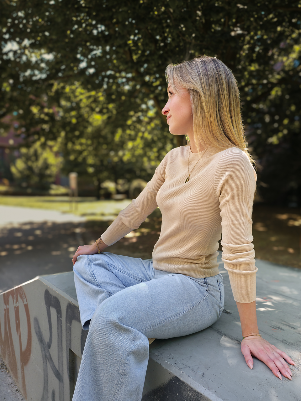 Seitliche Sitzansicht von Danja im beigen Merino-Longsleeve in XS im Park.